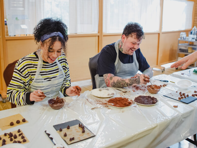 A couple are hand rolling truffles in a chocolate class.